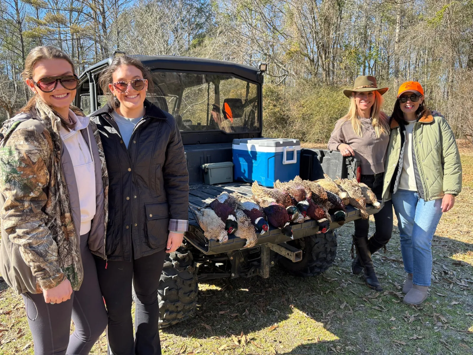 Four guests smiling beside a tailgate of harvested pheasants