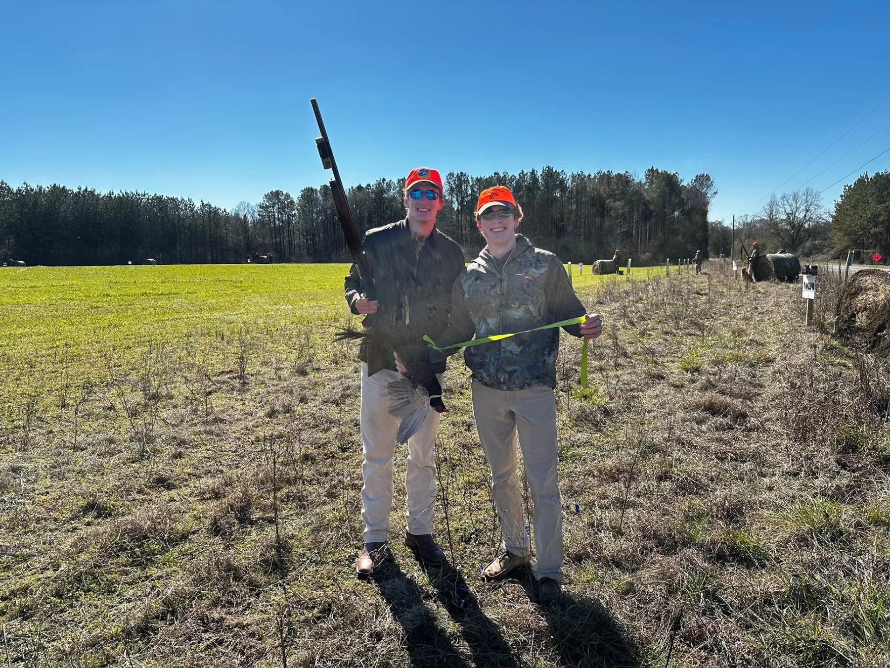Two young shooters holding a pheasant in an open field