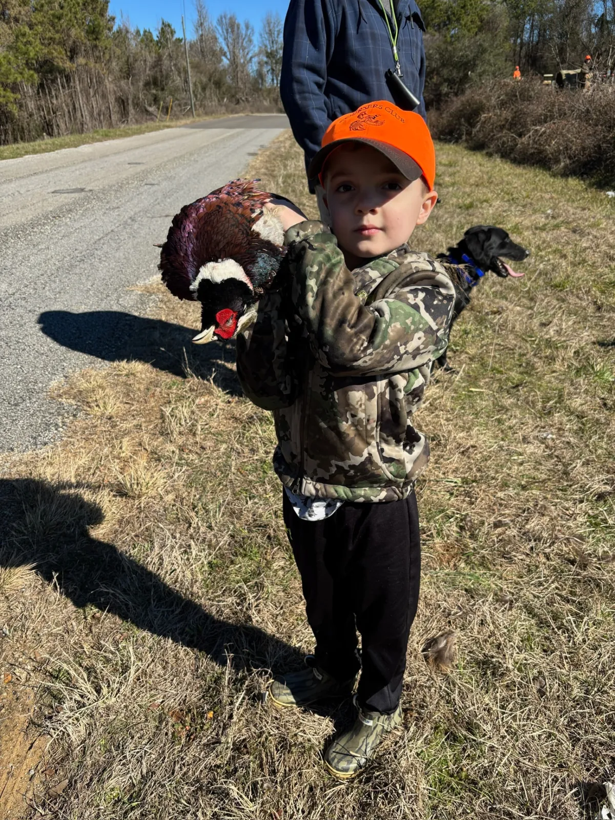 A young hunter in a Coursers Club orange cap carrying a rooster pheasant